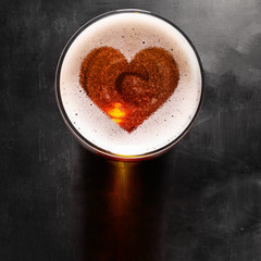 loving beer, heart symbol on foam in glass on black table, view from above