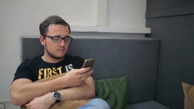 Bearded man with slightly disheveled hair chats in smartphone sitting in studio.
