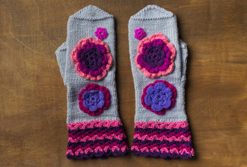 Gray mittens handmade on wooden surface with flowers. Flat lay