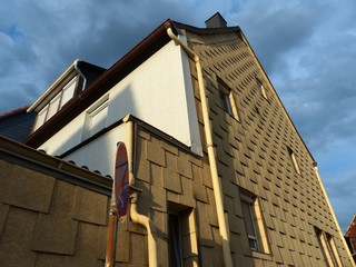 Sanierter Altbau mit Fassadenverkleidung ihn Beige und Naturfarben vor Wolkenhimmel im Sonnenschein...