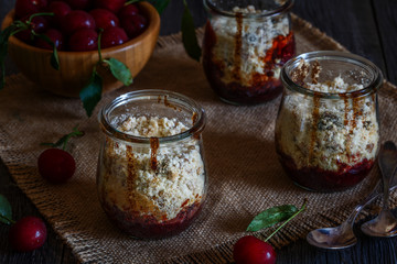 Homemade cherry crumble in glass jars on a dark wooden backgroun