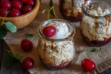 Homemade cherry crumble in glass jars on a dark wooden backgroun