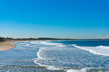 Beautiful ocean beach with moderate surf and broad waves against blue sky with a plane on the background. Cronulla, Australia. Copy space