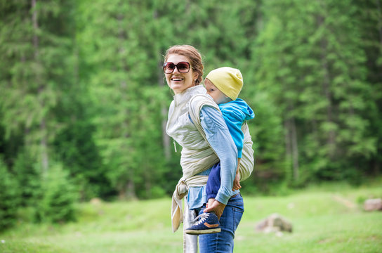 Young woman carrying her toddler son in woven wrap sling while hiking 