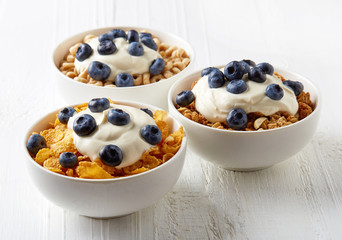 Three types of cereals with yogurt and blueberries on white tabl