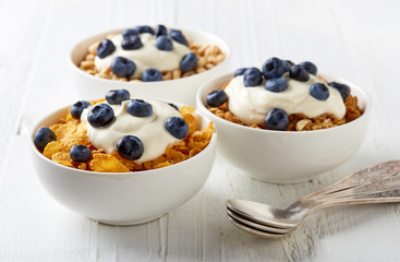 Three types of cereals with yogurt and blueberries on white tabl