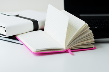 Opened paper notebook with blank sheets on white office table, laptop as background