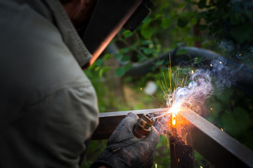 Worker in protective mask welding steel railings outdoors