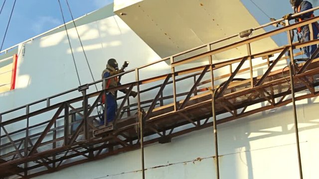 Shipyard Workers repairing and painting new layer of paint on modern ship