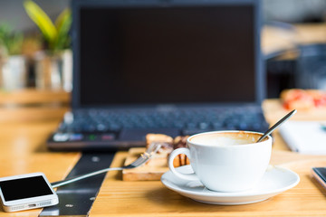 Laptop with cup of coffee and telephone on old wooden table.