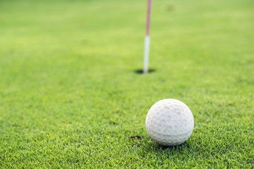 Golf ball on a green, in front of the hole, focus on the hole