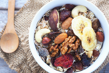 Top view of a bowl of muesli with oats, nuts and dried fruit on a sackcloth.