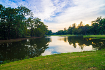 Sunset at summer park with beautiful green lawns pond