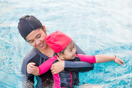 Young active mother having fun in a swimming pool with asian kid