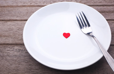 Top view of plate with decoration in the form of  red heart and fork on a wooden background.