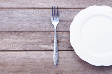 Top view of empty white plate with fork on a wooden background.