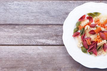 Top view of colorful of pasta on a white plate with wooden background.