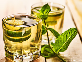 Alcohol drink. Wooden boards are two glasses with alcohol green transparent drink. Drink number two hundred ninety-two mojito cocktail with lime and mint leaf . Country life still. Light background.
