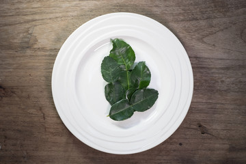 Kaffir lime leaves in ceramic dish on wood background.