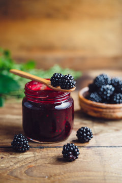 Fresh homemade blackberry jam in glass jar on a wooden background
