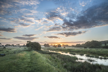 Beautiful vibrant Summer sunrise over English countryside landsc