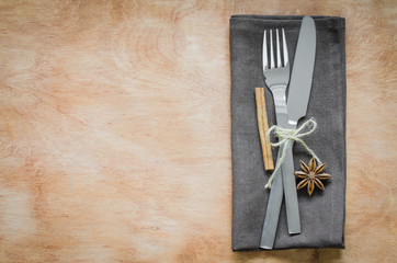 Close up Fork and Knife Tied on Brown Napkin Styled with cinnamon and anise, on Wooden Table.