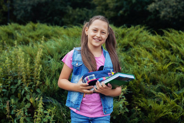 beautiful little girl standing in the yard with books and notebooks