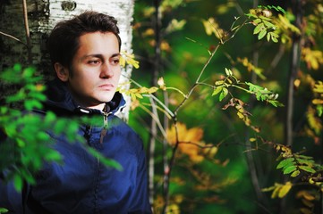 Young brown-eyed man with a sad face leaned against the birch tr