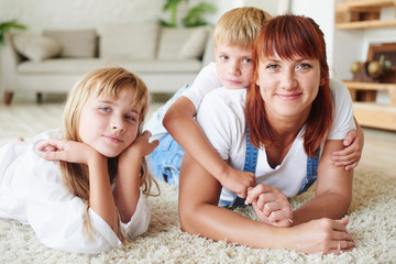 Portrait of mother with her daughter and son lying on the carpet on the floor of the house