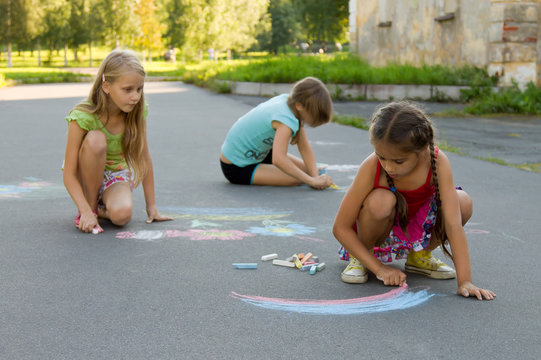 Three girl kids absorbedly drawing chalks on the pavement