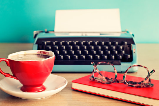 Turquoise typewriter, coffee cup and eyeglasses over red notebook