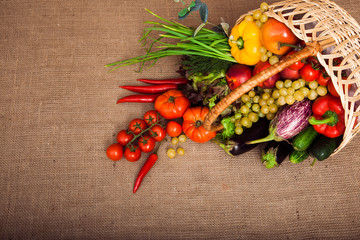 Healthy eating concept with mixture of organic vegetables, fruits and lettuce in wicker basket on kitchen table, covered Sack cloth at the background, copy space at below. Horizontal