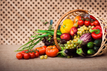 Fresh vegetables, fruits and lettuce in wicker basket on kitchen table, covered Sack cloth on a background of a wooden lattice, copy space at left. Healthy life concept. Horizontal