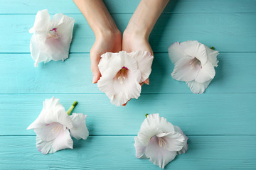 Fototapeta na wymiar Female hands holding gladiolus flower on wooden background