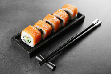 Sushi roll set in wooden plate and chopsticks on dark background