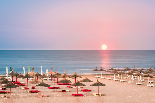 Clear sky sunrise over a sandy Black Sea beach, with straw umbrellas, in Romania