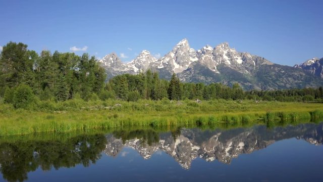 The water is perfectly smooth showing high peak reflections in the Teton's
