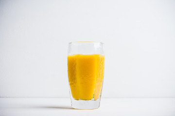 Glass of fresh orange juice on the white wooden background