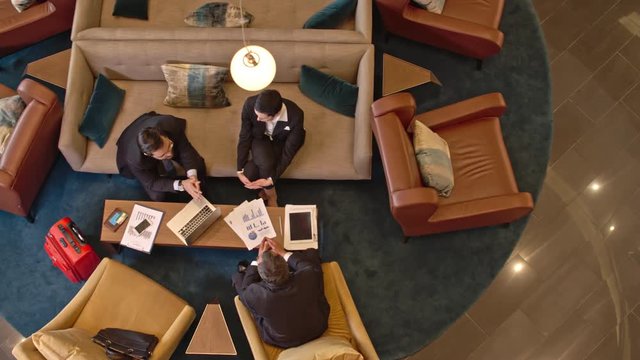 Directly above view of businessmen and businesswoman sitting in the hotel lobby and sharing ideas