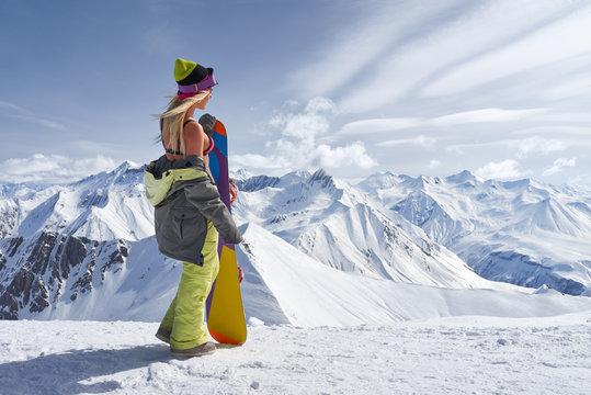 Back view of girl with colorful snowboard looking away mountains