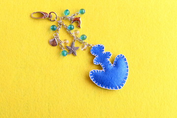 Anchor charm keychain for beach bag. Blue felt anchor keychain with beads isolated on a yellow...