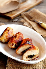 Small stuffed Turkey meat rolls on a plate. Fork, cuisine board on old wooden table. Roasted Turkey breast rolls with cheese and agaricus. Festive food recipe. Rustic style. Vertical photo