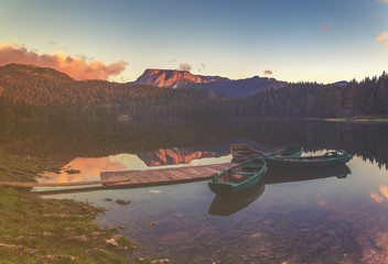 łódki zacumowane przy drewnianym pomoście nad pięknym,górskim jeziorem,kolorystyka retro
