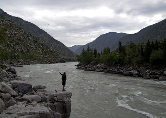 man standing on a large rock spread his arms over mountain river