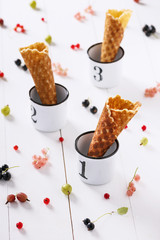 Empty homemade ice cream cones in white enamel cups with mix of berry fruits. Selective focus.