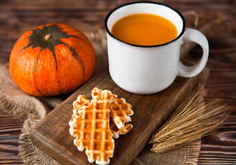 Mug of fresh pumpkin juice with wafer and pumpkin on dark wooden