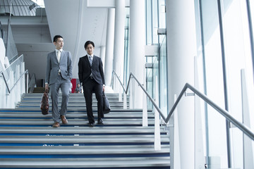 Two businessmen are down the stairs of the office