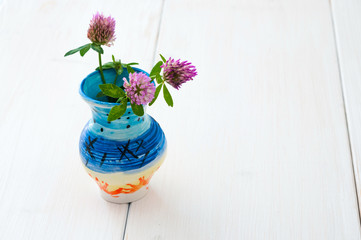 Three clover flowers in ceramic jug on white wooden table