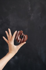 Chocolate donut in a woman's hand on black background