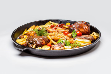 Meat assortment on a large frying pan, potato slices braised cabbage and tomatoes. On a white background